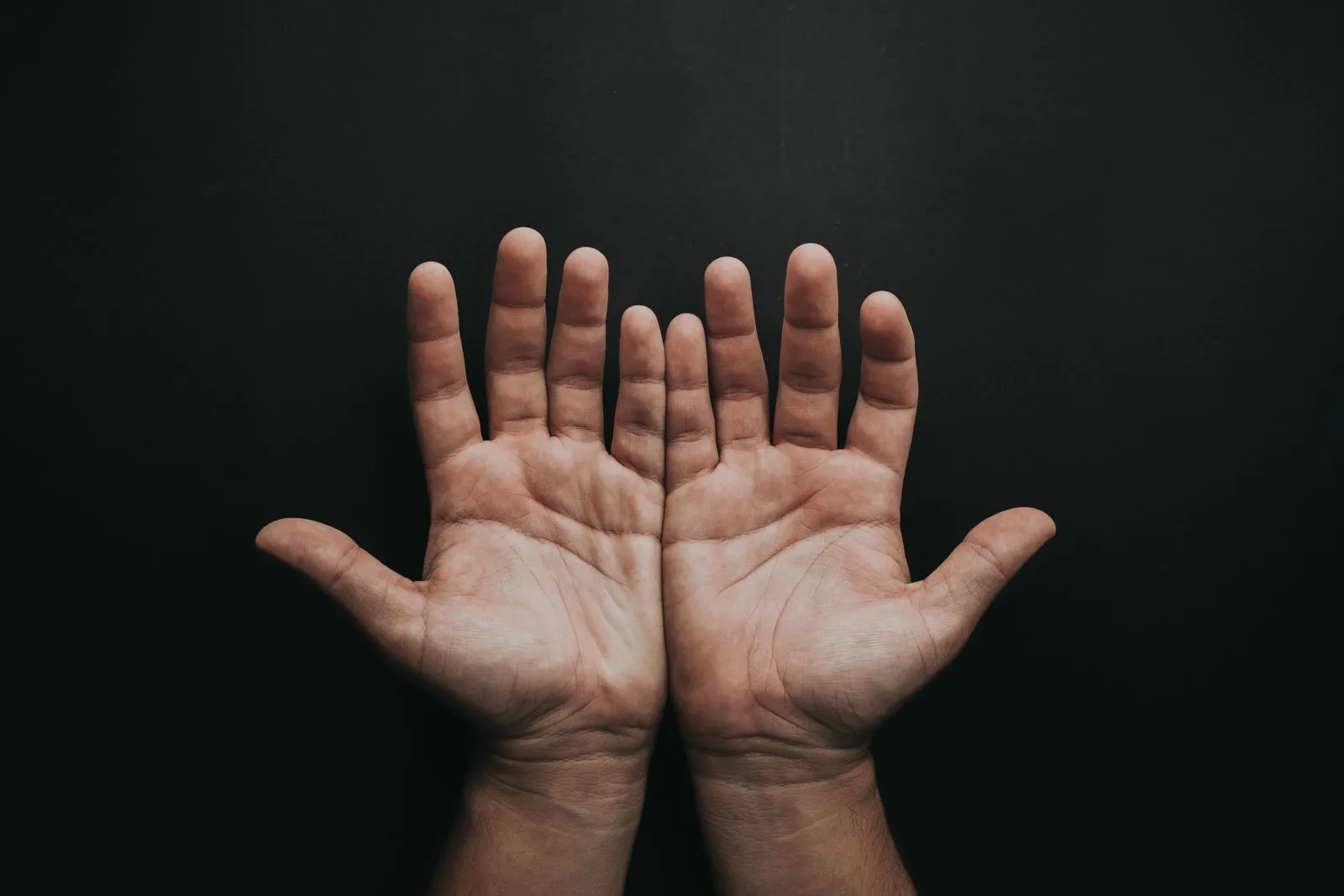 Two open palms against a dark background with fingers and skin creases clearly visible