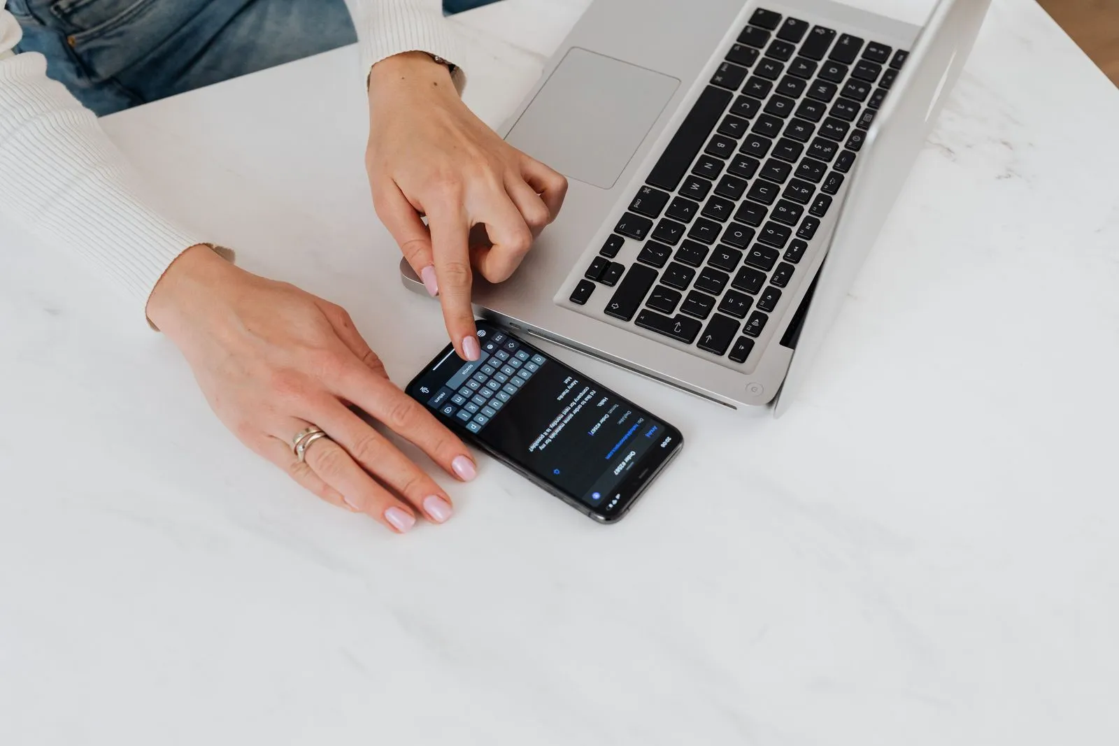 Hands on a smartphone and a laptop on a white desk