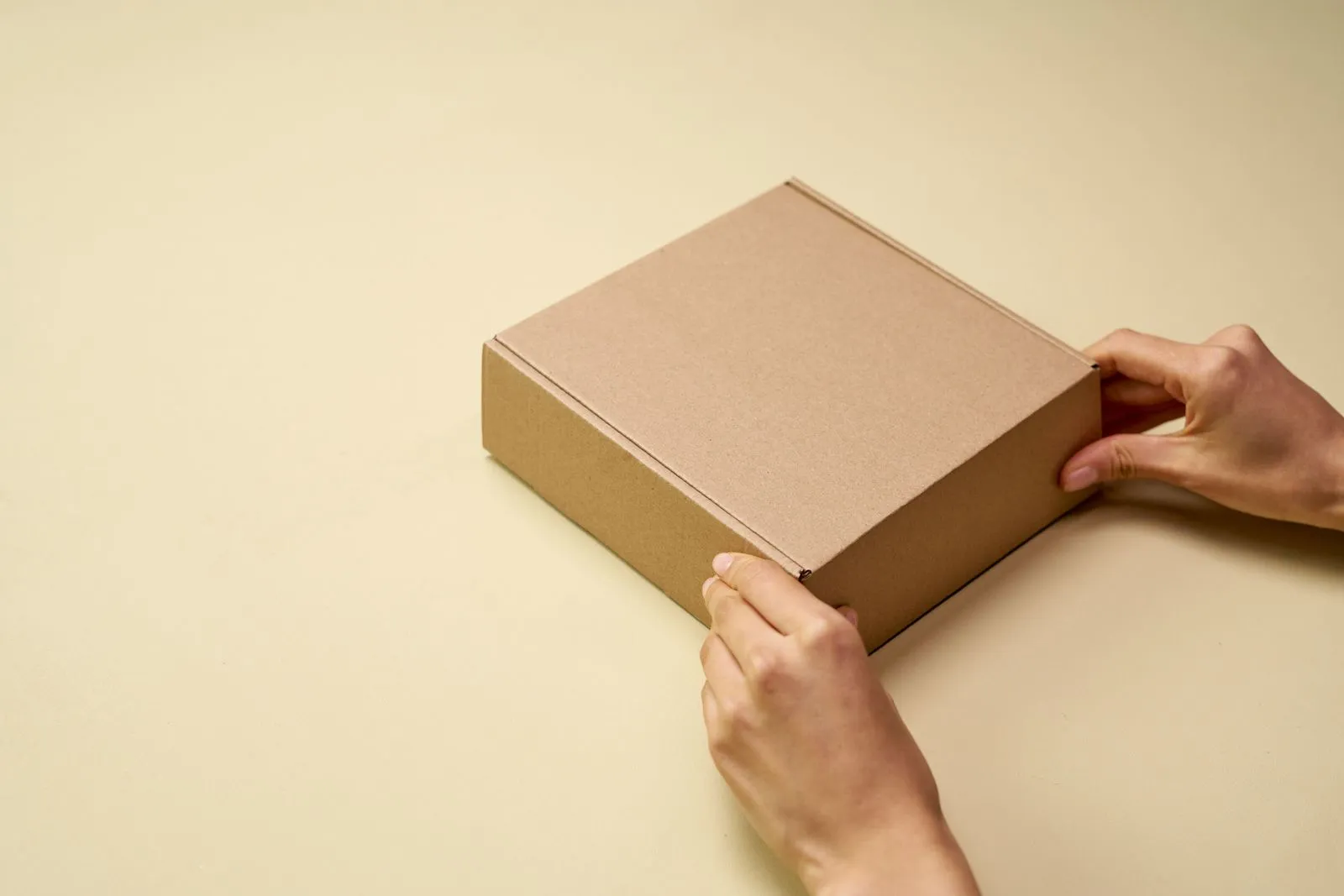 Two hands hold a plain brown cardboard shipping box on a light table