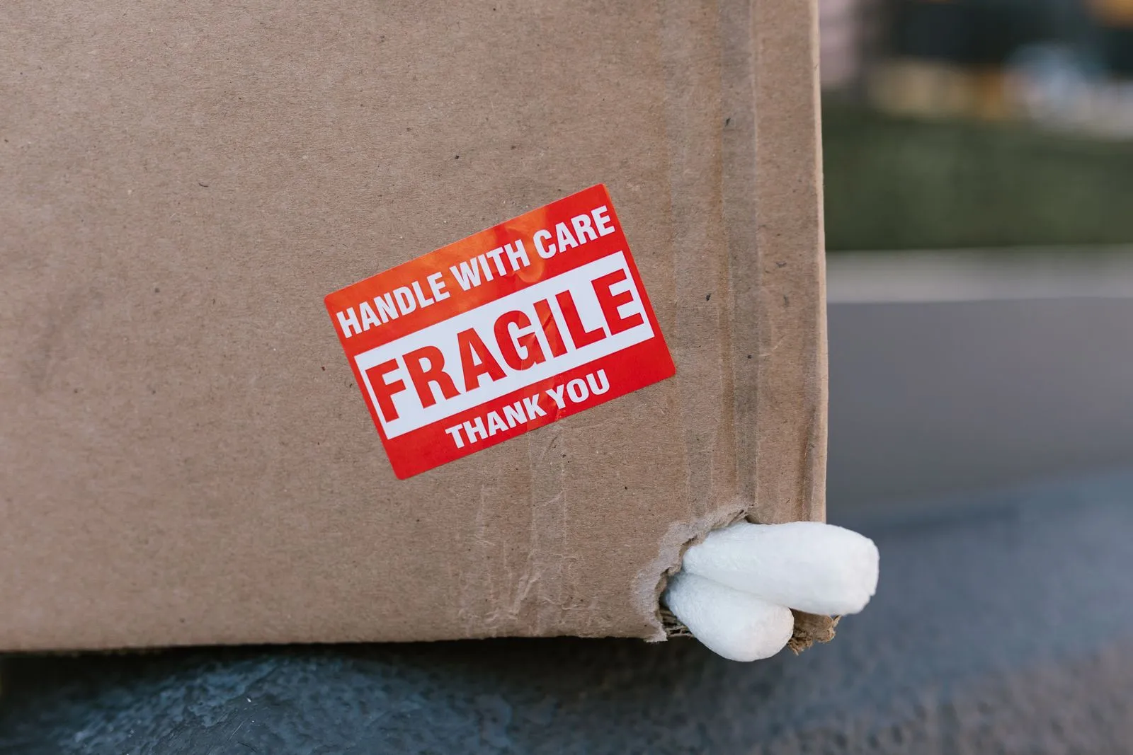 Cardboard box with a fragile sticker and a torn corner with packing peanuts spilling out
