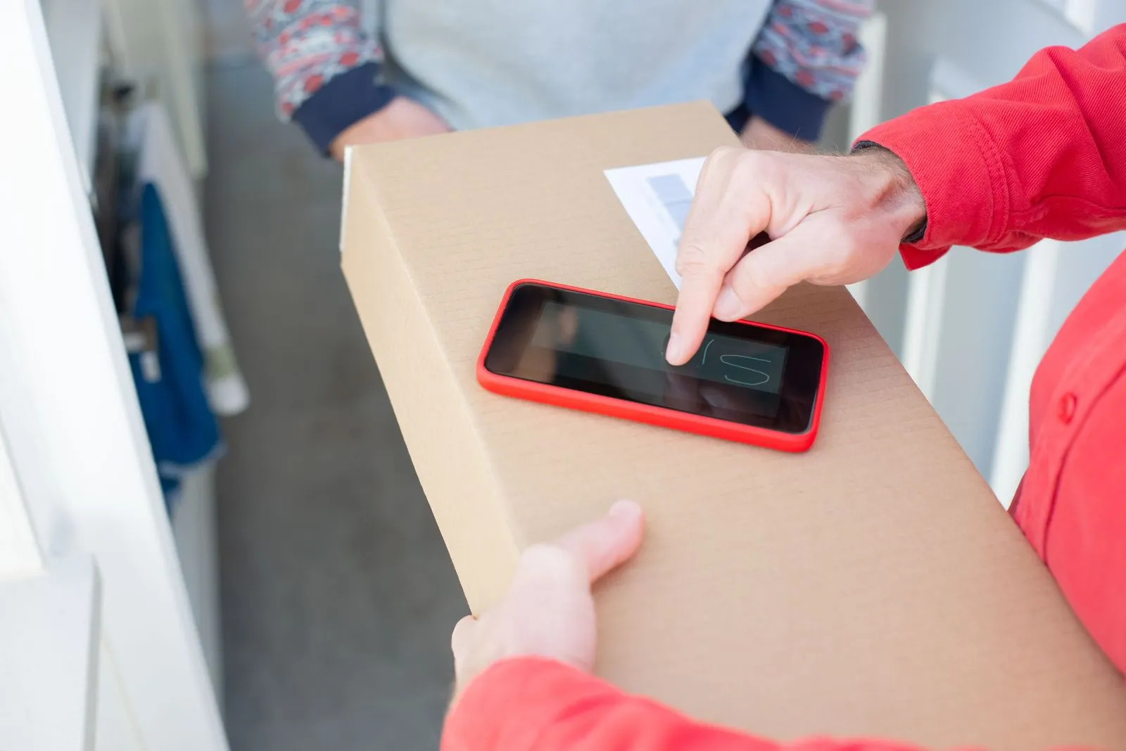 Hands holding a shipping box with a smartphone on top for a delivery signature