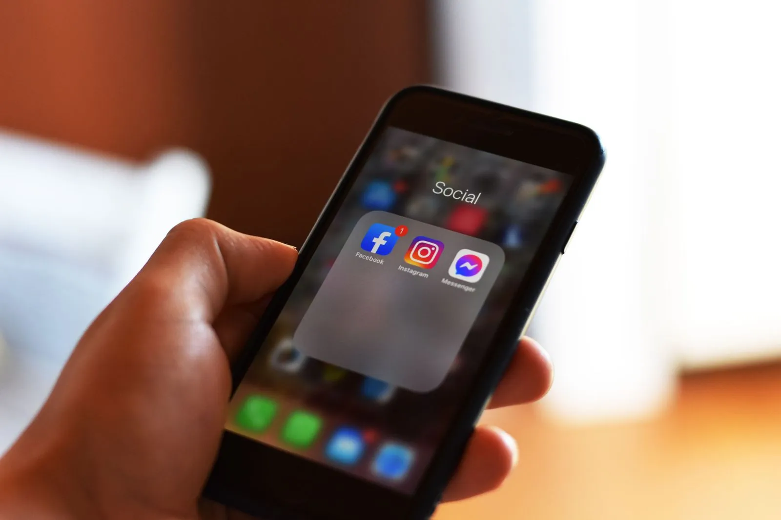 A hand holding a smartphone with a folder containing the Facebook, Instagram and Messenger apps