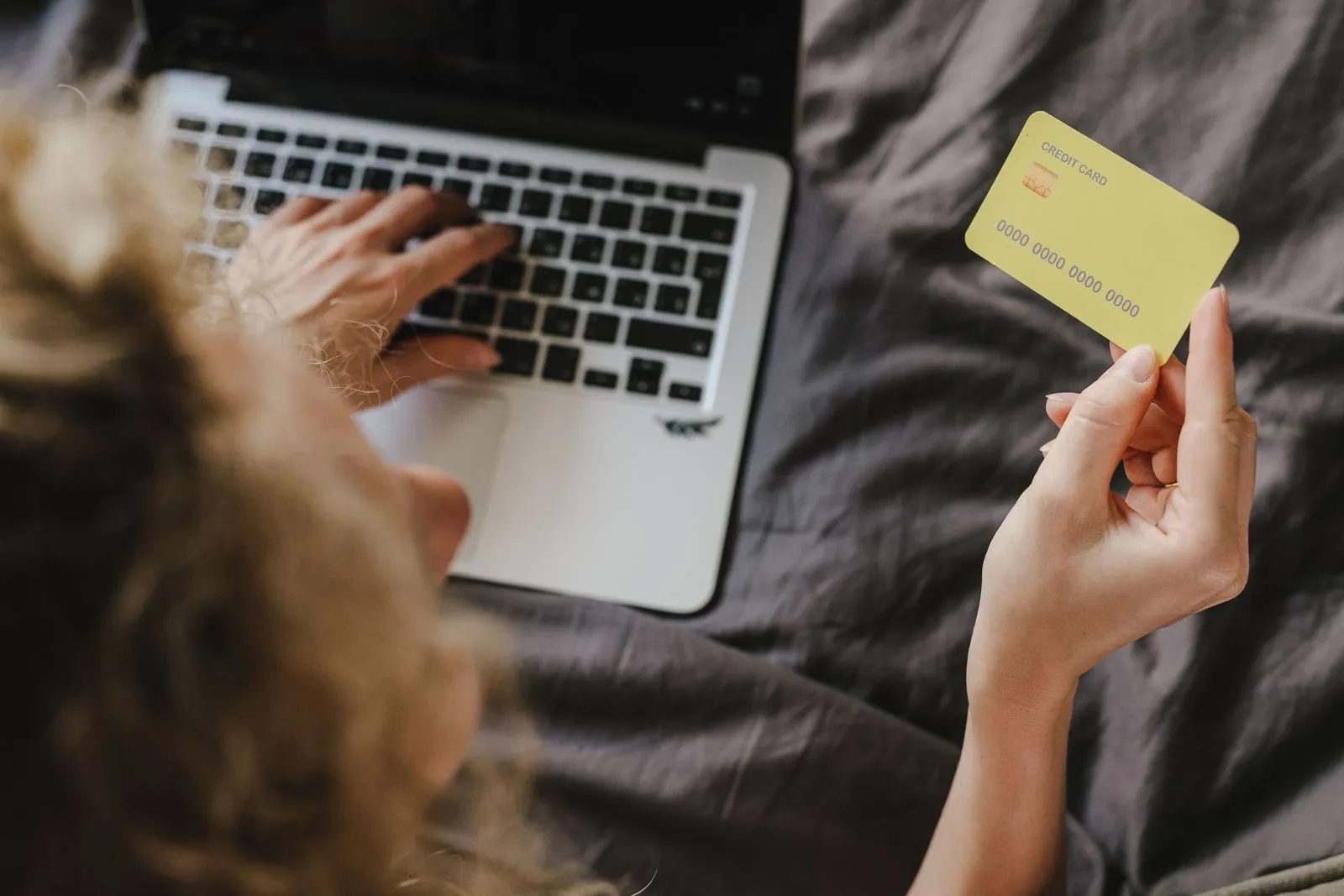 A hand types on a laptop while the other hand holds a credit card