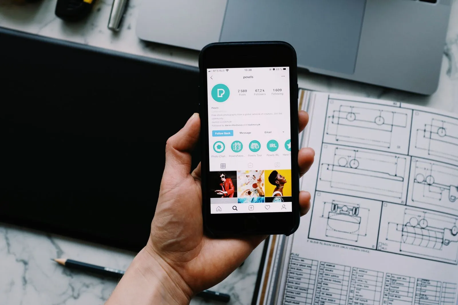 A hand holds a smartphone showing an open social media profile above a desk