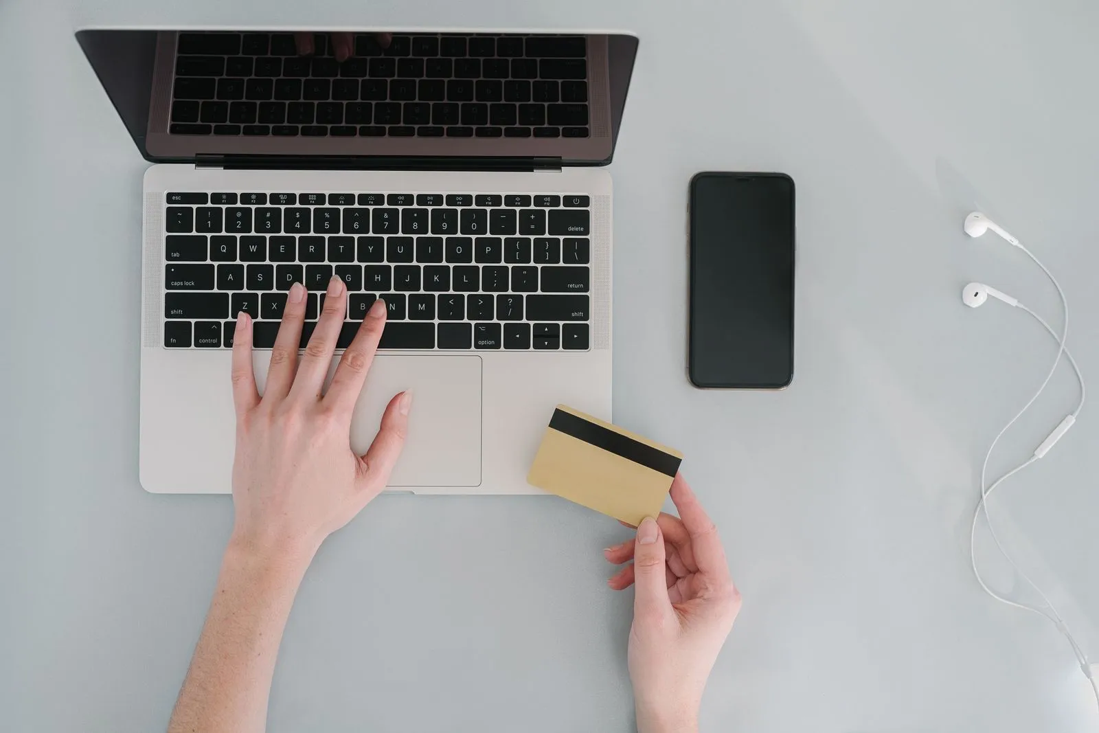 Hands on a laptop, one holding a gold bank card, with a smartphone on the desk beside it