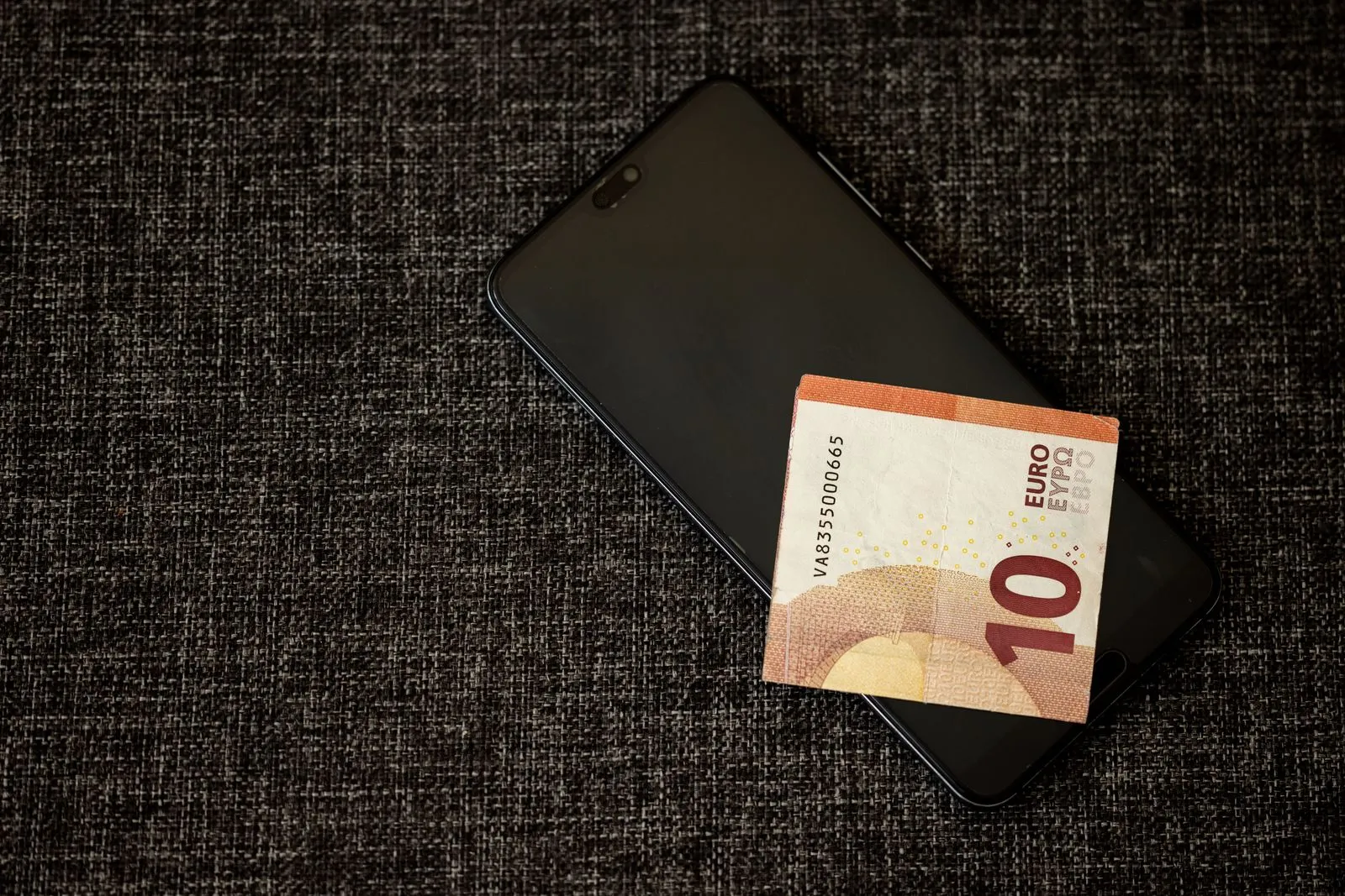 Ein Zehn-Euro-Schein liegt auf einem Smartphone auf dunklem Stoff