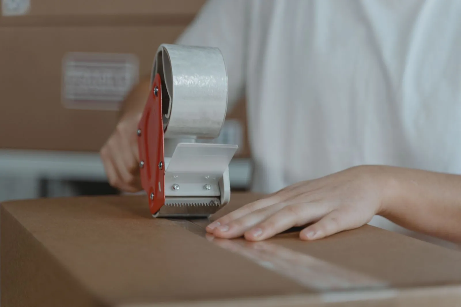 Hands sealing a cardboard shipping box with packing tape