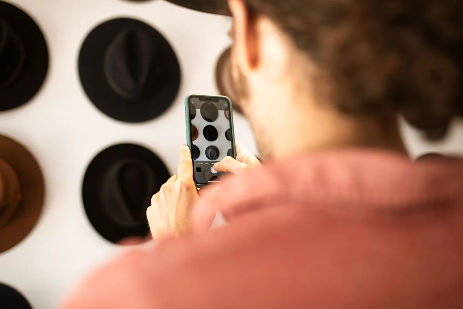 Person photographing hats on a wall with a smartphone