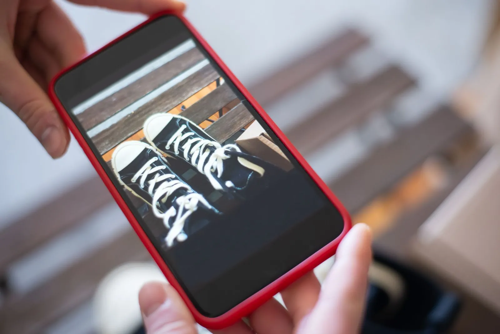 Hands photographing a pair of black sneakers with a smartphone