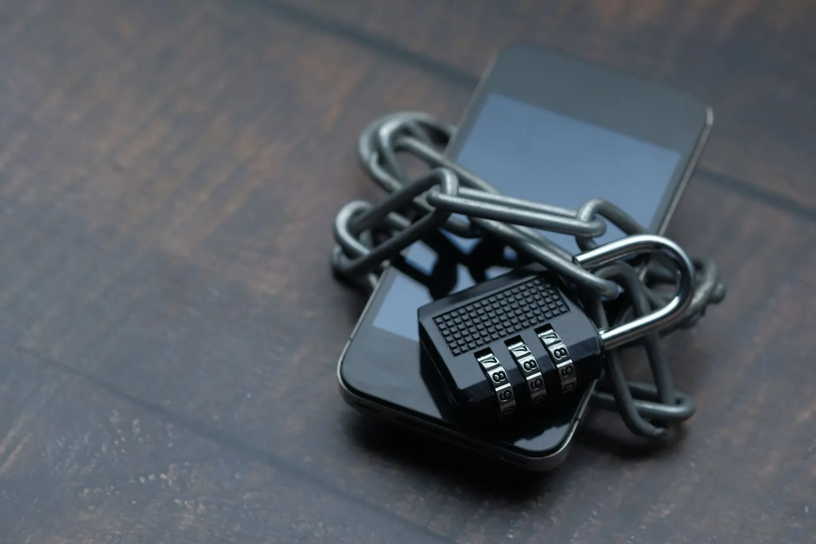 Smartphone wrapped in a metal chain with a combination padlock on a wooden table