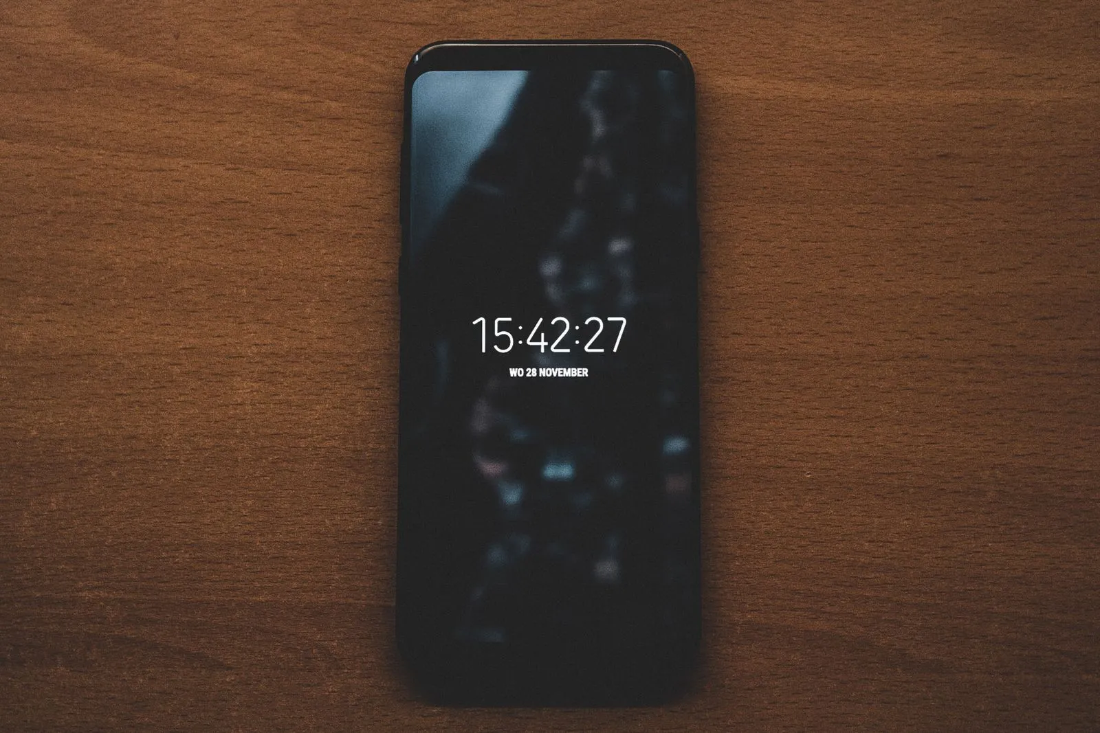 Smartphone lying on a wooden table, its screen showing the time and date